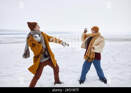 Ritratto a tutta lunghezza di coppia giocando a palla di neve lotta all'aperto in inverno, copia spazio Foto Stock