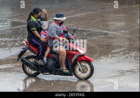 SAMUT PRAKAN, THAILANDIA, ottobre 03 2022, due donne cavalcano una moto in forte pioggia con bambini piccoli protetti da una borsa di plastica sulla testa Foto Stock