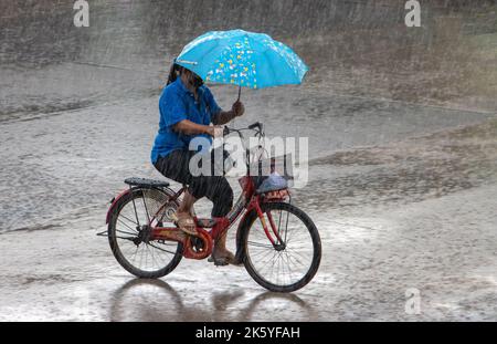 SAMUT PRAKAN, THAILANDIA, ottobre 03 2022, Una donna guida una bicicletta con un ombrello in mano Foto Stock