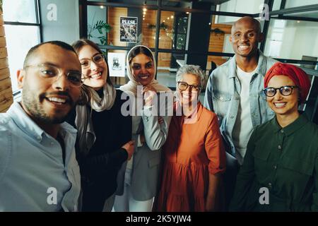 Colleghi di lavoro felici sorridendo alla macchina fotografica mentre prendono un selfie del personale. Gruppo di uomini d'affari multiculturali che eseguono una startup di successo in un Foto Stock