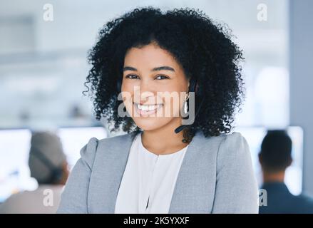 Ritratto di un giovane agente di telemarketing del call center che parla con le cuffie mentre lavora in un call center con i suoi colleghi nel Foto Stock