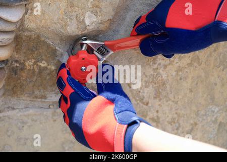 Le mani maschili nei guanti protettivi riparano il rubinetto con una chiave speciale Foto Stock