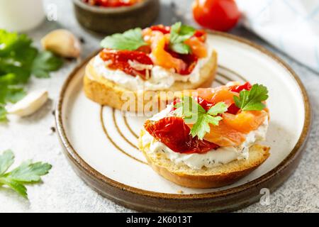 Panini aperti o bruschetta con salmone salato, formaggio e pomodoro essiccato al sole su un tavolo di pietra. Cibo sano, frutti di mare. Foto Stock