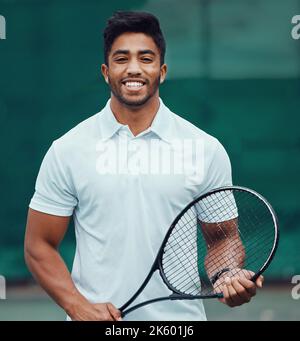 Ritratto di un tennista indiano sorridente che tiene un racket su un campo. Felice fit sport etnico professionista in piedi da solo e sentirsi fiduciosi in un Foto Stock
