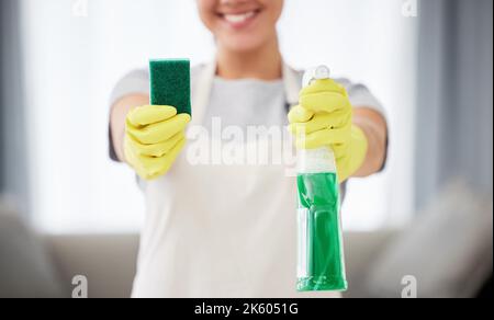 Una donna irriconoscibile che tiene un prodotto di pulizia e una spugna mentre pulisce il suo appartamento. Un detergente domestico sconosciuto che indossa guanti di pulizia in lattice Foto Stock