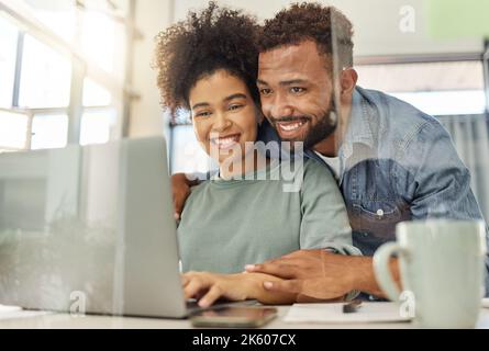 Giovane coppia felice di gara mista che lavora insieme su un portatile al tavolo di casa. Allegro fidanzato ispanico e fidanzata pianificazione e la lettura di un Foto Stock