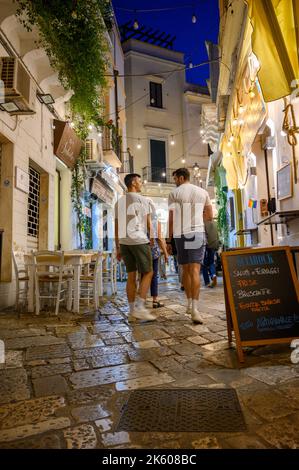 Turisti e locali a piedi lungo una tipica strada stretta e acciottolata nel centro storico di Gallipoli in serata, Puglia, Italia. Foto Stock