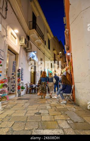 Turisti e locali a piedi lungo una tipica strada stretta e acciottolata nel centro storico di Gallipoli in serata, Puglia, Italia. Foto Stock