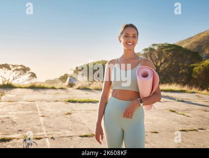 Ritratto di donna yoga che tiene tappeto yoga dopo pratica all'aperto nella natura remota al tramonto. Bello sorridente giovane caucasico in piedi da solo. Uno felice Foto Stock