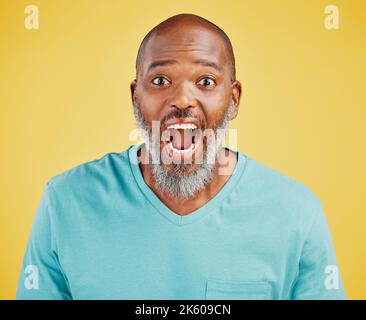 Uomo africano maturo che guarda sorpreso contro uno sfondo giallo studio. Ragazzo nero che esprime shock e incredulità con la bocca aperta. Reagire Foto Stock