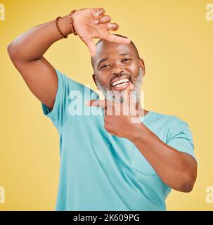 Ritratto di un felice uomo africano maturo che fa un gesto di cornice con le mani su uno sfondo giallo studio. La vita è piena di momenti felici e noi Foto Stock