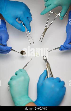 Igiene orale dentale. I dentisti tengono la varietà di attrezzi metallici per l'odontoiatria medica intorno ad un dente. Primo piano delle mani dei dentisti nei guanti che trattengono l'ammaccatura Foto Stock