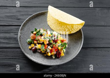 Salsa con mais e fagioli su uno sfondo di legno con tacos. Cucina messicana Foto Stock