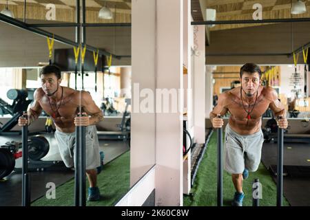 L'uomo trascina il peso in una palestra accanto a uno specchio con la sua immagine riflessa su di esso Foto Stock