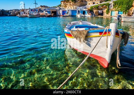 Colorato autentico peschereccio greco ancorato in un piccolo villaggio in acque cristalline. Garage imbiancati, cielo blu, mare, colline. Milos, Grecia Foto Stock