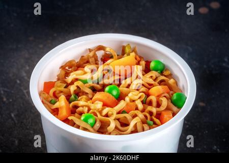 Tazza di ramen, spaghetti istantanei di soba in una tazza di plastica con verdure, piselli verdi e carote, colpo di primo piano Foto Stock