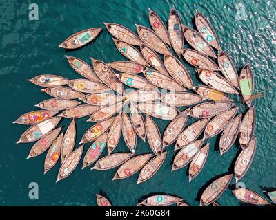 Dhaka, Dhaka, Bangladesh. 11th Ott 2022. Una flotta di barche in legno, che assomigliano ai petali di fiori, attende per i pendolari del traghetto attraverso il fiume Buriganga per lavorare in un porto fluviale importante a Dhaka, Bangladesh, mentre i barcaioli legano insieme le barche in un modello fiorito e ottenere quaranta verri davanti all'ora di punta pomeridiana. Lavorano 16 ore al giorno e ottengono meno di Â £ 5 per questo. Quindi, si riposano ogni volta che hanno la possibilità di alleviare la fatica delle lunghe ore di lavoro. Durante quel periodo, la maggior parte delle barche sono legate insieme tranne alcune e il numero di passeggeri è più basso rispetto a t Foto Stock