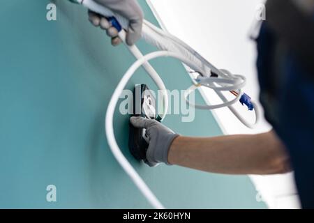 Tecnico maschile, elettricista o costruttore utilizza un moderno misuratore di lunghezza laser. Primo piano della mano dell'uomo nei guanti protettivi che si collegano alla parete tra i fili e. Foto Stock