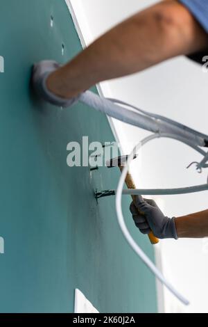 Primo piano del chiodo martellante nella parete. L'operatore maschio guida i perni nella parete prima di installare il condizionatore d'aria. Vista dal basso ad angolo delle mani che tengono hamme Foto Stock