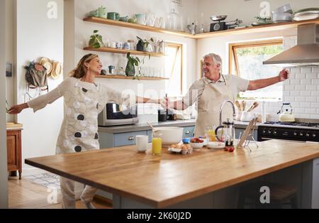 Coppia anziana, ballare in cucina e sorridere con amore mentre si fa colazione frittella in casa di famiglia. Buon vecchio, ballando con una donna anziana sorridente Foto Stock