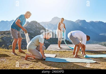 Gruppo di uomini e donne diversi che arrotolano i loro materassini di yoga dopo una lezione di gruppo in montagna. Vivere uno stile di vita attivo e sano Foto Stock