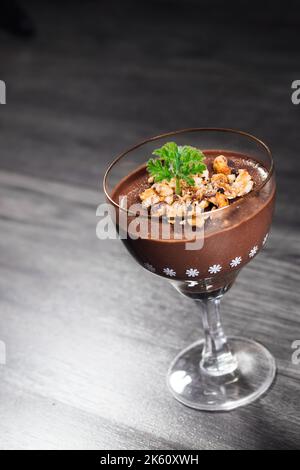 Budino al cioccolato decorato con nocciole schiacciate e foglie di geranio commestibili (fuoco selettivo) Foto Stock