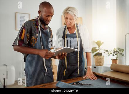 Due progettisti che utilizzano un tablet digitale mentre lavorano con il materiale al lavoro. Giovane afroamericano su misura parlare e tenere un tablet digitale mentre Foto Stock