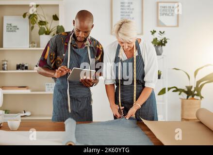 Due progettisti che utilizzano un tablet digitale mentre lavorano con il materiale al lavoro. Giovane afroamericano su misura parlare e tenere un tablet digitale mentre Foto Stock