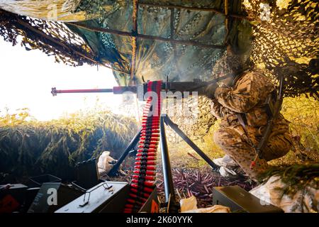 Soldati in primo piano che sparano una pistola Cal Machine 50 con ottone esaurito intorno ad essa. Foto Stock