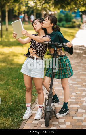 Le ragazze nel parco che guardano qualcosa in linea e che osservano interessate Foto Stock