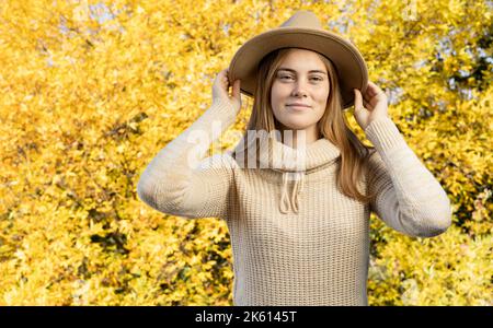 Ritratto di una bella ragazza in cappello con capelli lisci lunghi su sfondo lievito. maglione a maglia in autunno Foto Stock