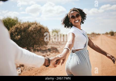 Coppia, camminando e natura con una donna nera e un uomo all'aperto tenendo le mani su una strada di sabbia in un dessert insieme. Viaggi, amore e romanticismo con un Foto Stock