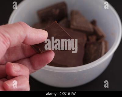 Un uomo che tiene in mano un pezzo di cioccolato fondente rotto. Primo piano. Foto Stock