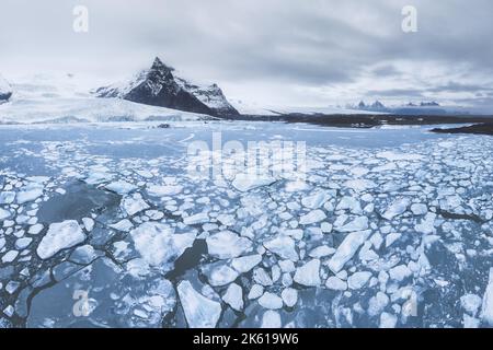 Scenario mozzafiato di montagne rocciose coperte di neve vicino lago ghiacciato contro cielo nuvoloso nel Parco Nazionale di Vatnajokull Foto Stock