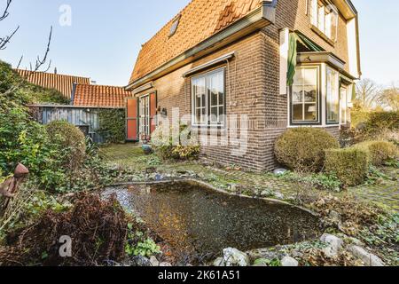 Casa in mattoni con patio pulito lastricato con piccolo giardino e stagno e. Foto Stock