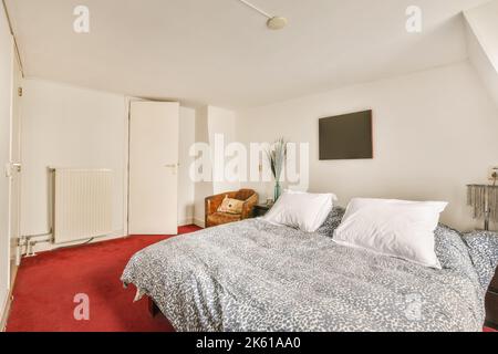 Comodo letto posto su tappeto rosso con poltrona in pelle in camera da letto chiara in appartamento Foto Stock