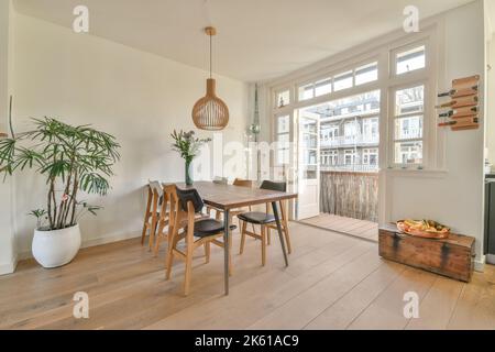Sedie poste a tavolo quadrato con pianta in vaso in una luminosa e spaziosa sala da pranzo con finestre e porte in vetro in appartamento Foto Stock