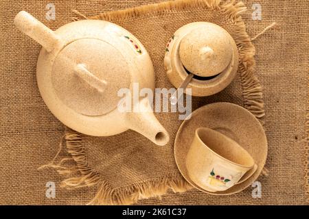 Una tazza di argilla su un piattino, teiera e ciotola di zucchero su un panno di iuta, macro, vista dall'alto. Foto Stock