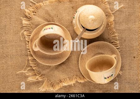 Due tazze di argilla su un piattino, una ciotola di zucchero su un panno di iuta, macro, vista dall'alto. Foto Stock