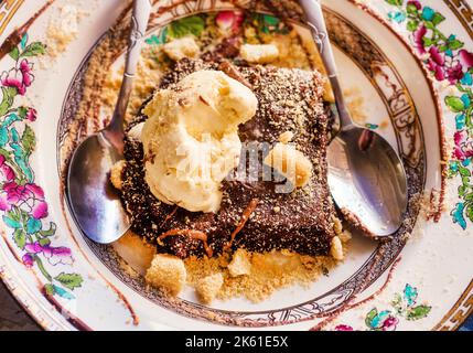 Brownie al cioccolato fondente con gelato servito con due cucchiai su un piatto rustico tradizionale Foto Stock