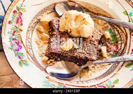 Brownie al cioccolato fondente con gelato servito con due cucchiai su un piatto rustico tradizionale Foto Stock