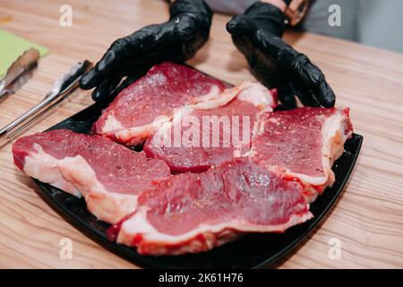 Manzo crudo affettato, preparazione di carne per la cottura della bistecca alla lezione di cucina. Carne cruda su un piatto nero. Foto Stock