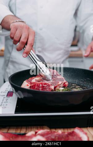 cottura delle bistecche in padella. cottura del manzo alla lezione di cucina. le mani dello chef in guanti neri. Foto Stock