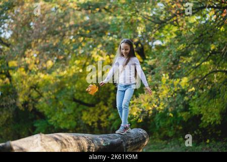 La ragazza carina bilancia su un ceppo caduto con una foglia nella sua mano nel parco. Foto Stock