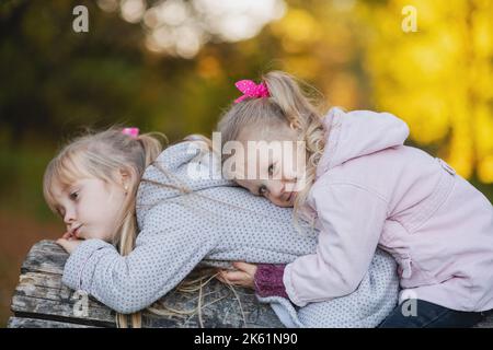 Due simpatiche bambina si trova su un tronco caduto nel parco e sorride. Ritratto di una bambina sorridente sdraiata sul dorso della sorella. Foto Stock