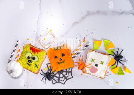 Cibo per bambini, feste o colazione Halloween idea. Semplice ricetta di panini sani da pane tostato, avocado, formaggio cremoso, zucca spalmata con Halloween Foto Stock