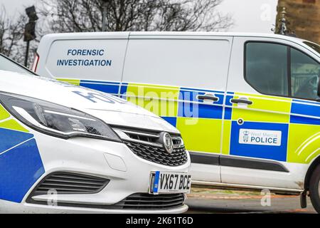 Vista laterale bassa dei veicoli della polizia parcheggiati senza agenti all'interno. Un'indagine forense firmata furgone è sullo sfondo. Foto Stock