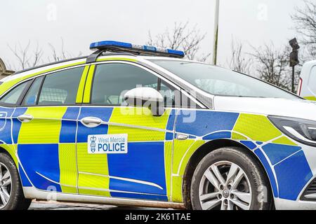 Bassa pov/angolo, vista laterale (fuori-lato) di auto di polizia appartenente alla forza di polizia di Mercia Occidentale UK, con alto-vis blu e giallo battenburg marcature parcheggiate. Foto Stock