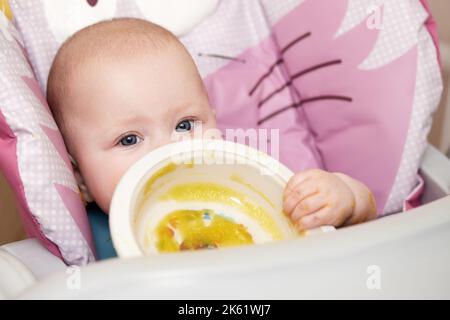 bambina che mangia con il cucchiaio in cucina Foto Stock