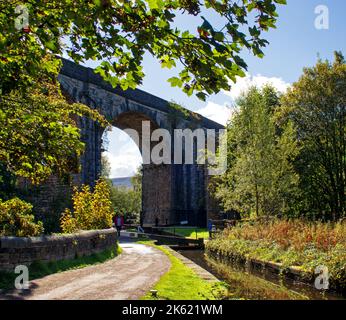 Guardando lungo il sentiero sotto uno storico viadotto ferroviario, lungo una serratura sul canale stretto di Huddersfield, a Uppermill, Oldham, Foto Stock